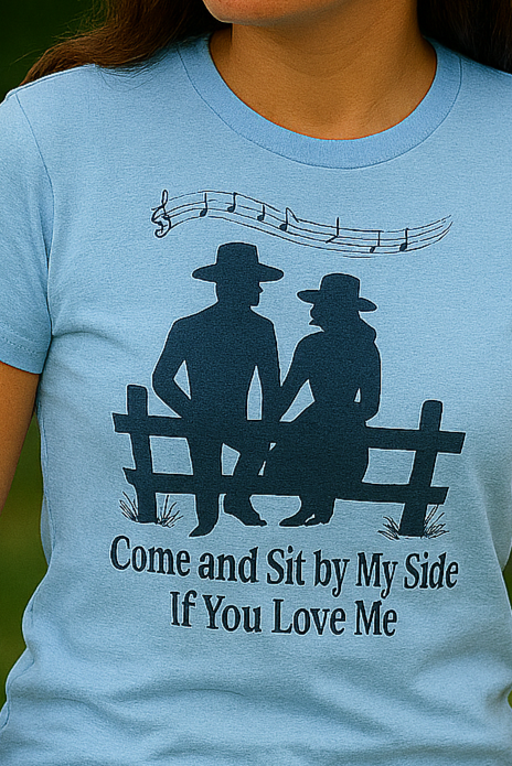 Cowgirl in baby blue tee leaning on a rustic fence, surrounded by lush greenery with a contemplative expression.
