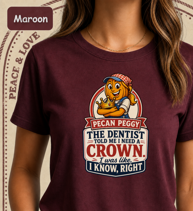 A woman wearing a maroon short-sleeve graphic T-shirt. The shirt features a cartoon peach character and the text 'PECAN PEGGY THE DENTIST TOLD ME I NEED A CROWN.