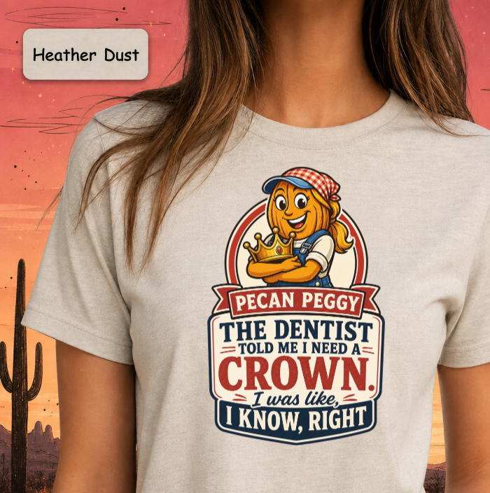 A person wearing a light heather dust graphic T-shirt with a large cartoon corn character and text that reads, 'Pecan Peggy The Dentist Told Me I Need a Crown. I was like, I Know, Right.
