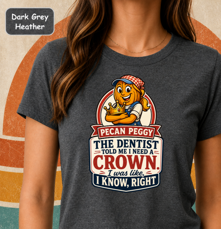 A woman wearing a dark grey heather graphic t-shirt featuring a cartoon pecan character named Peggy and a humorous dental joke. The top-left corner has a label reading 'Dark Grey Heather'.