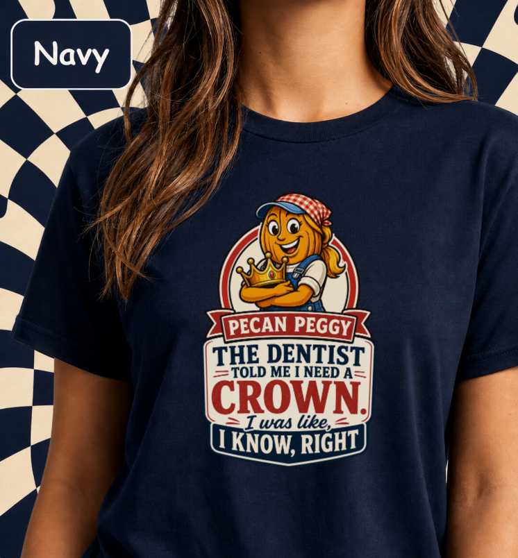 A navy blue graphic t-shirt worn by a model. The shirt features a cartoon illustration of 'Pecan Peggy' the pecan mascot with a crown, and a humorous dental slogan.