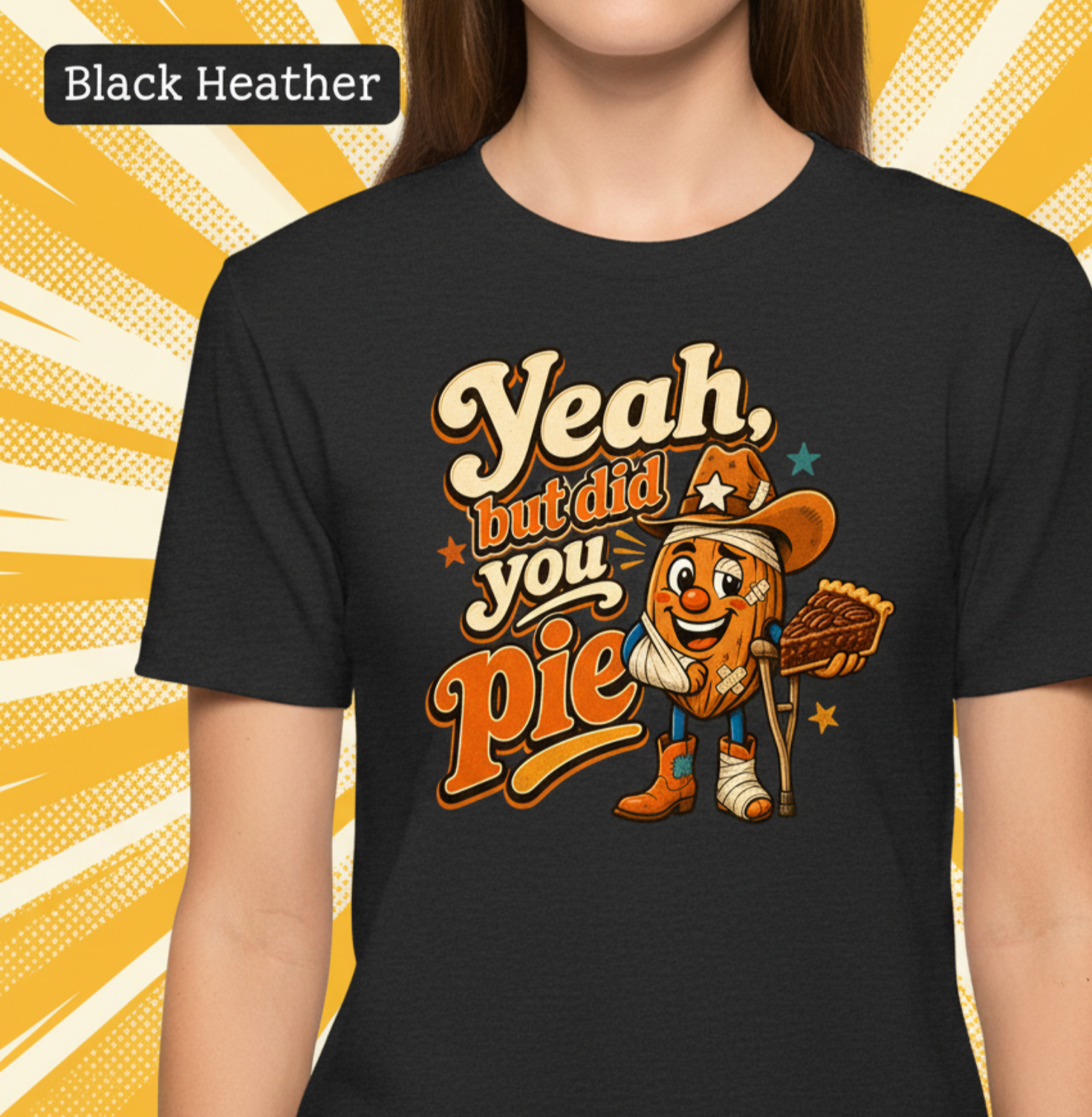 A person wearing a black heather short-sleeve t-shirt with a colorful graphic that reads 'Yeah, but did you pie' featuring a cartoon pie character in cowboy boots holding a slice of pie. The background is yellow and white with a 'Black Heather' label in the top left corner.