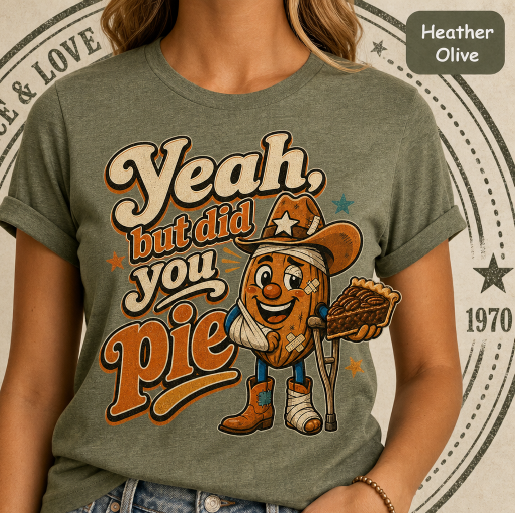 A person wearing a heather olive green graphic T-shirt with a cartoon potato character holding a pie slice and the text 'Yeah, but did you pie.' A color label in the top right reads 'Heather Olive.