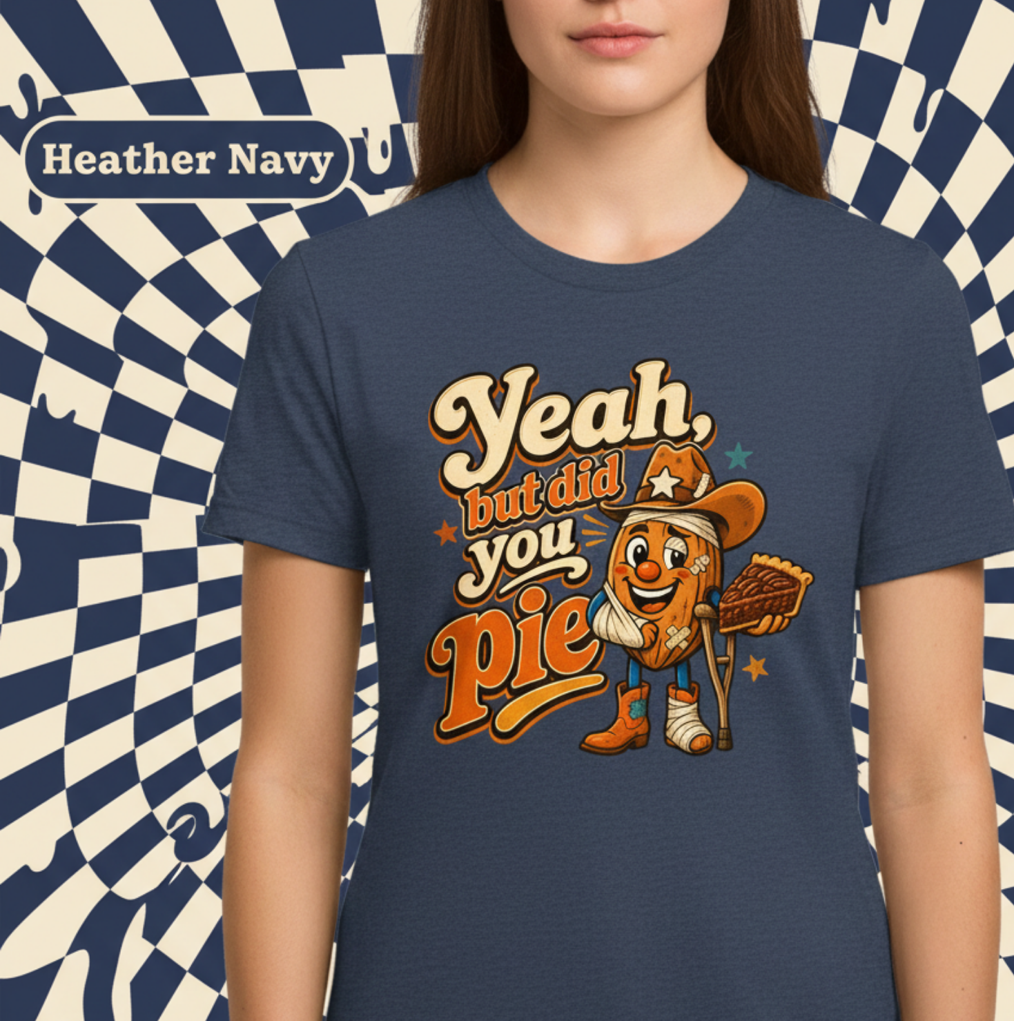 A person wearing a heather navy graphic T-shirt with a large retro-style print reading “Yeah, but did you pie” and a cartoon pie character holding a baseball glove. The background is a blue-and-white checkerboard swirl pattern, and a label in the upper left reads “Heather Navy.