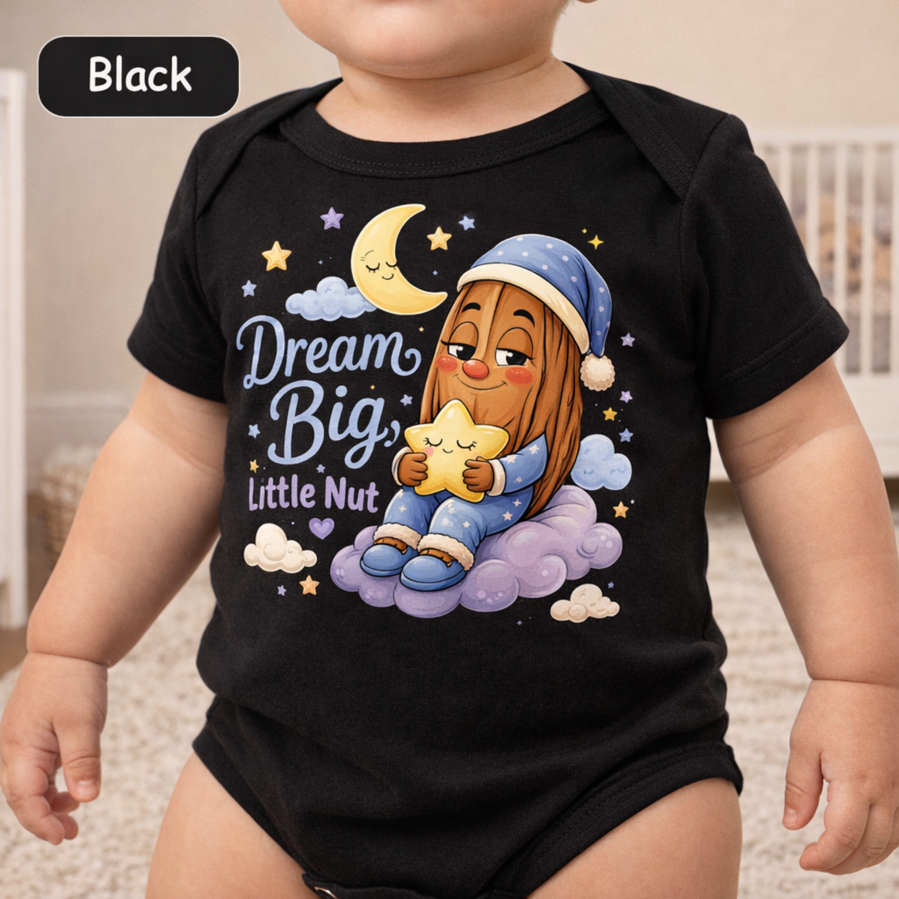 A baby wearing a black short-sleeve bodysuit with a colorful cartoon graphic of a child nut under a crescent moon and stars, with the text 'Dream Big, Little Nut'.