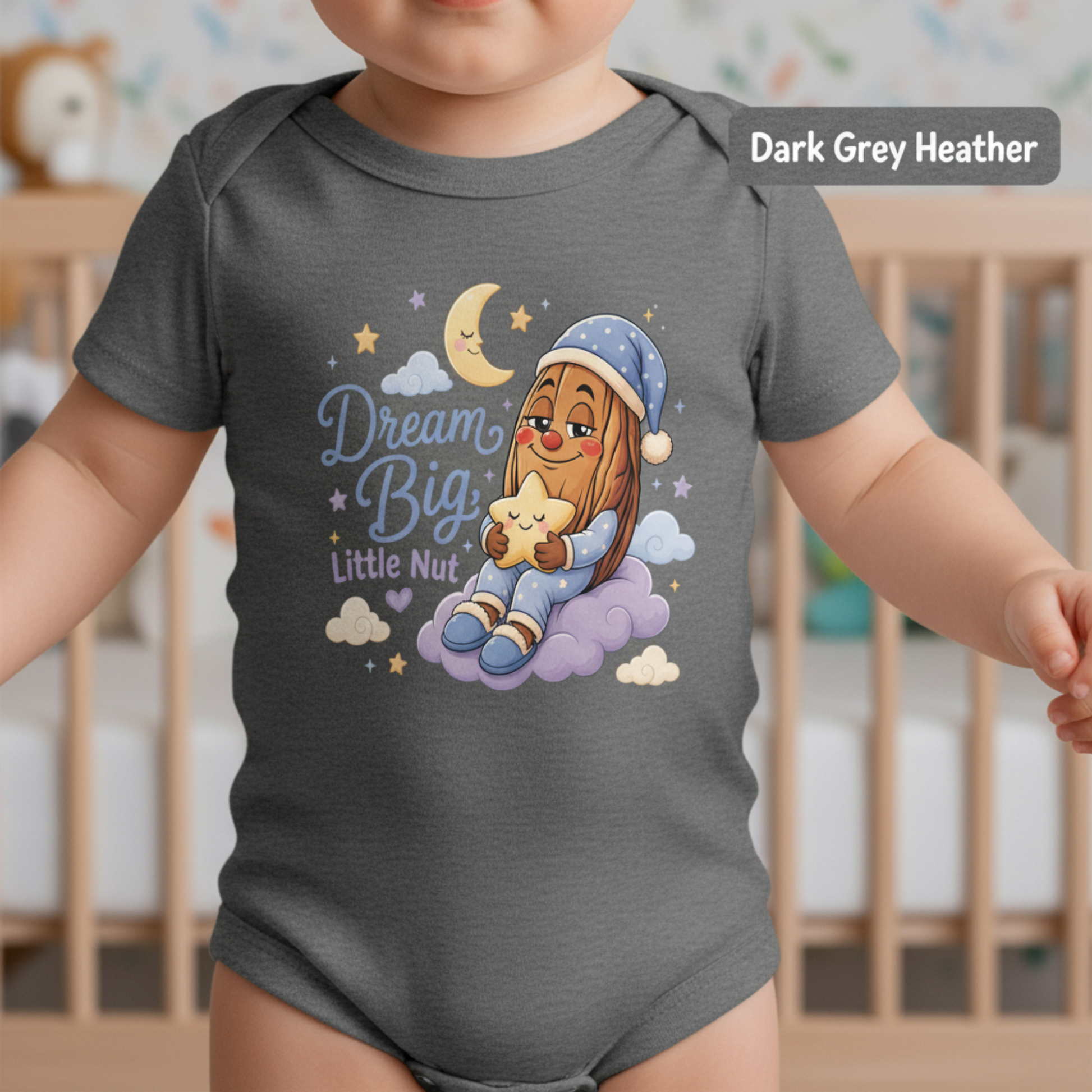 A baby wearing a dark grey heather short-sleeve bodysuit with a colorful cartoon graphic of a bearded nut holding a star under a crescent moon and the words 'Dream Big Little Nut'.