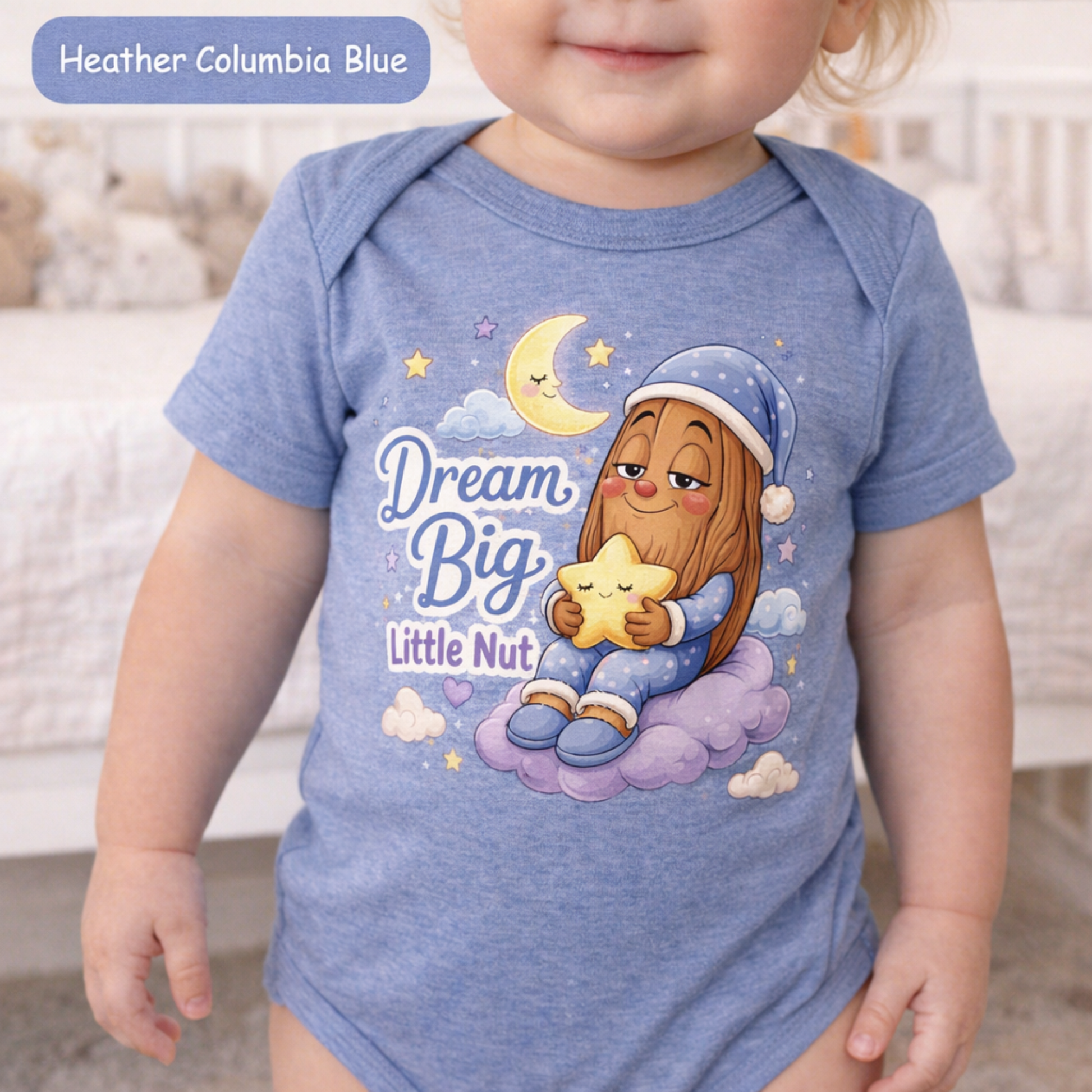 A baby wearing a heather blue short-sleeve bodysuit with a cartoon graphic of a girl holding a star under the text 'Dream Big Little Nut'. A blue label in the top left reads 'Heather Columbia Blue'.