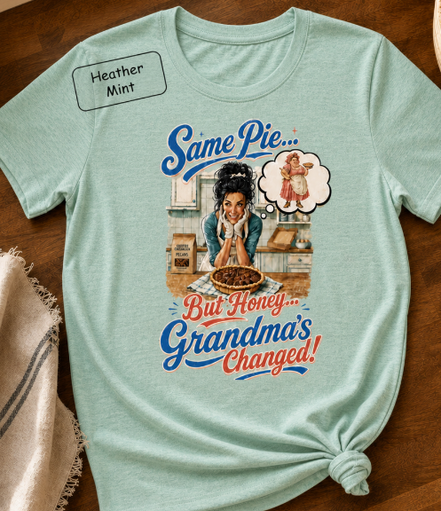 Bella+Canvas t-shirt displaying a graphic of a modern, stylish grandma in a kitchen reflecting on traditional grandmas, with retro typography reading "Same Pie, Grandma's Changed".