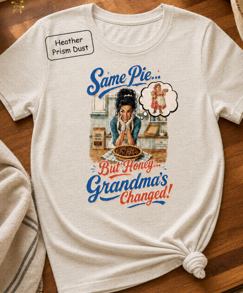 Bella+Canvas t-shirt displaying a graphic of a modern, stylish grandma in a kitchen reflecting on traditional grandmas, with retro typography reading "Same Pie, Grandma's Changed".