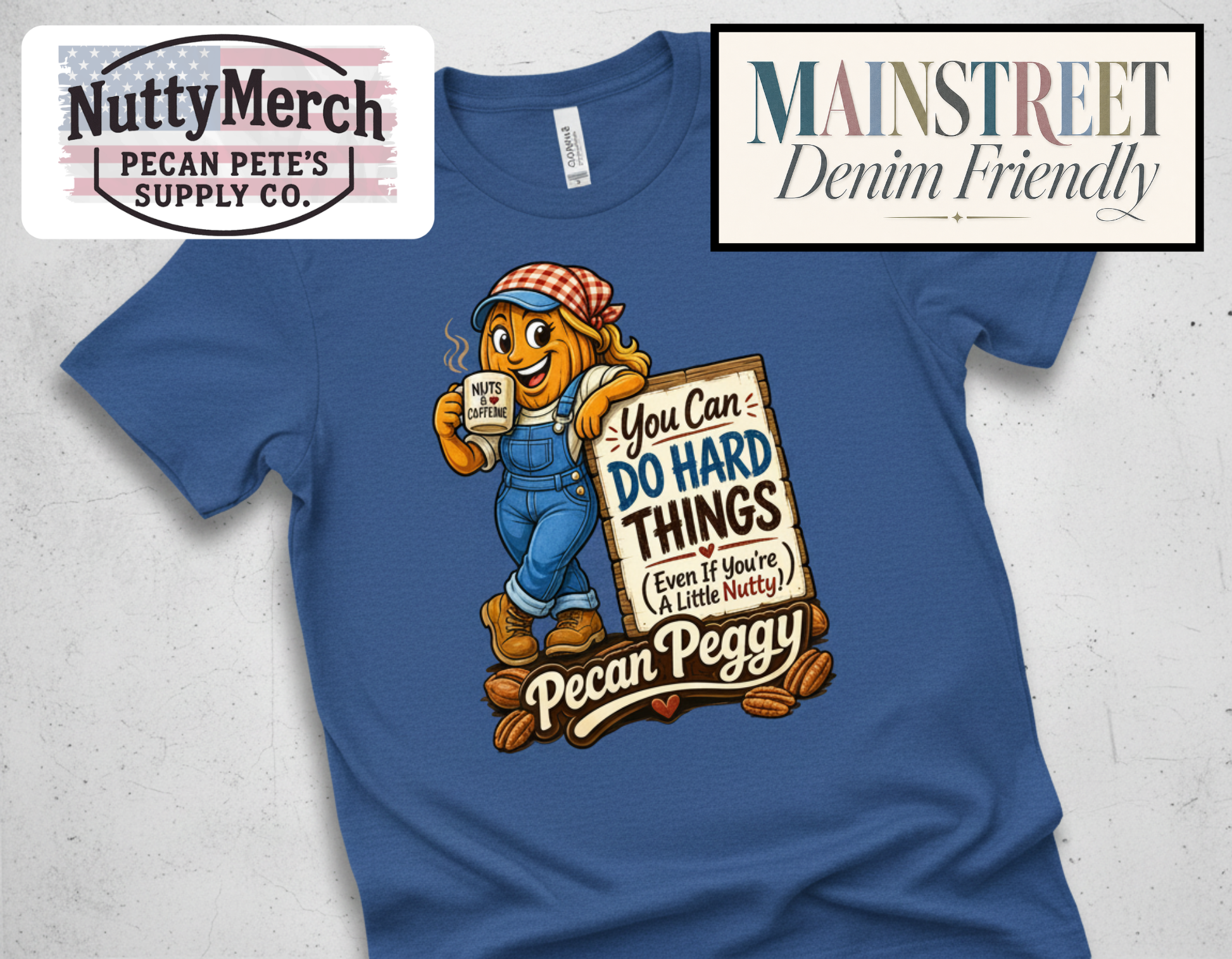 A blue short-sleeve graphic T-shirt laid flat on a light textured background. The shirt features a cartoon peach character wearing blue overalls and a red-and-white checkered hat, holding a mug and a sign that reads, 'You Can DO HARD THINGS (Even if You're A Little Nutty!)' with 'Pecan Peggy' written below.