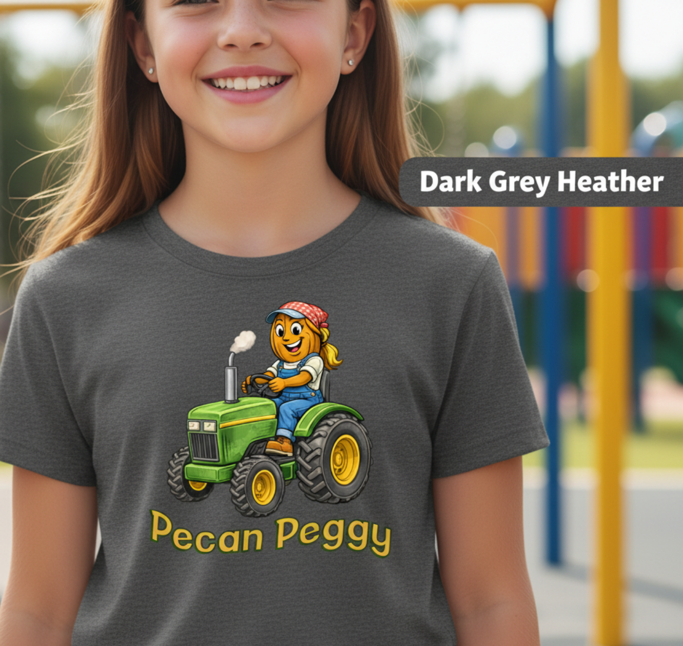 Child wearing a t-shirt with a cartoon character on a tractor and 'Pecan Peggy' text, standing in front of playground equipment.