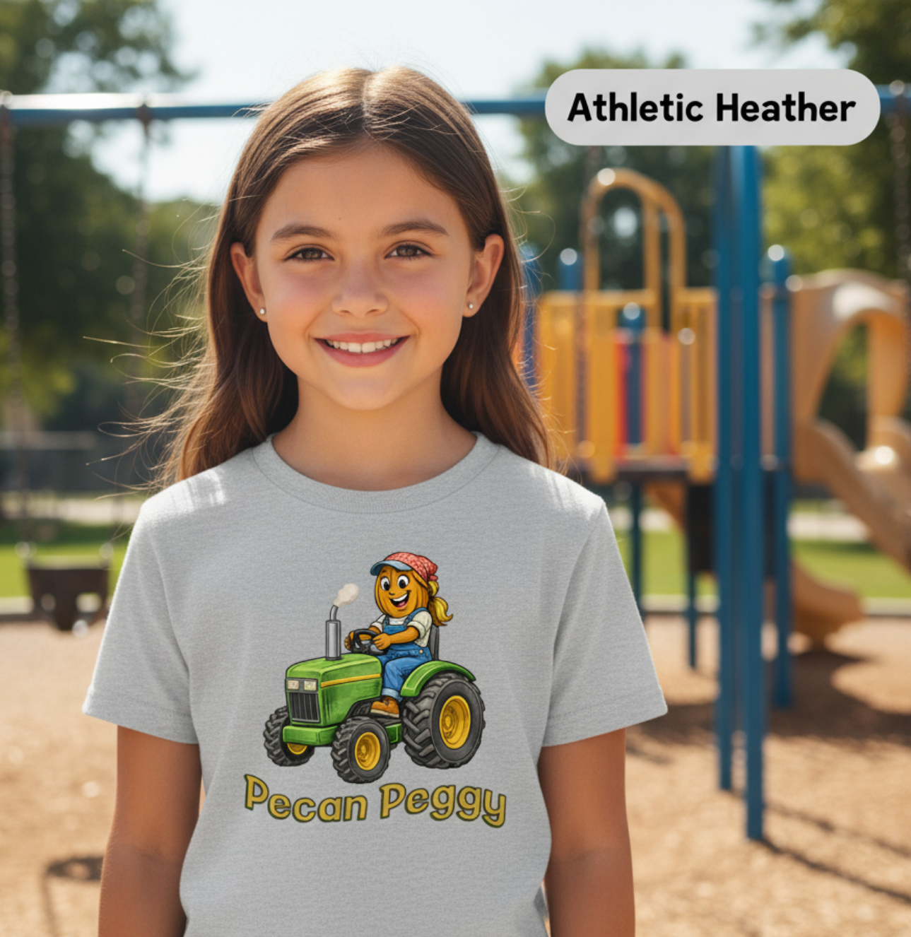 Girl wearing a t-shirt with a cartoon character and 'Pecan Peggy' text on a green tractor at a playground.
