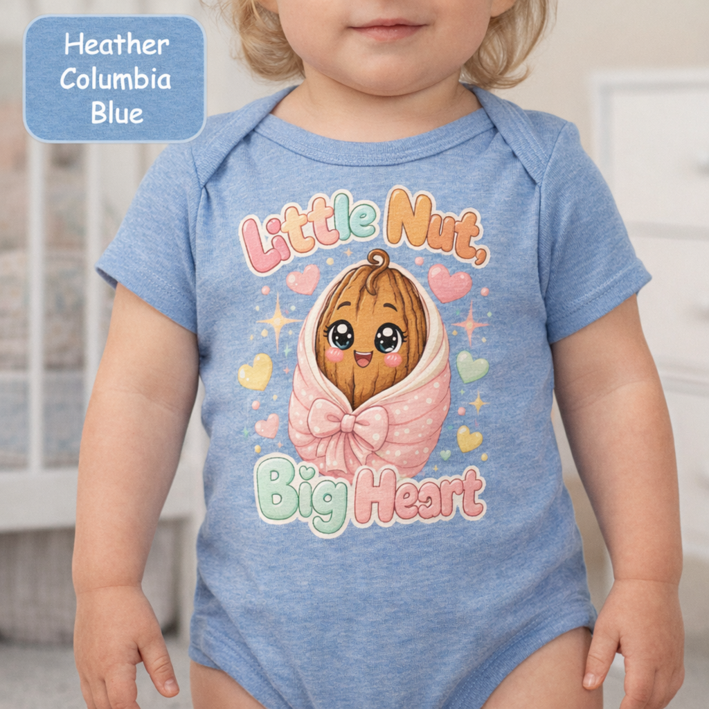 A baby wearing a heather blue short-sleeve bodysuit with a cute graphic of a smiling nut character wrapped in a pink bow, surrounded by pastel hearts and the words 'Little Nut, Big Heart.' A blue label in the top left reads 'Heather Columbia Blue.