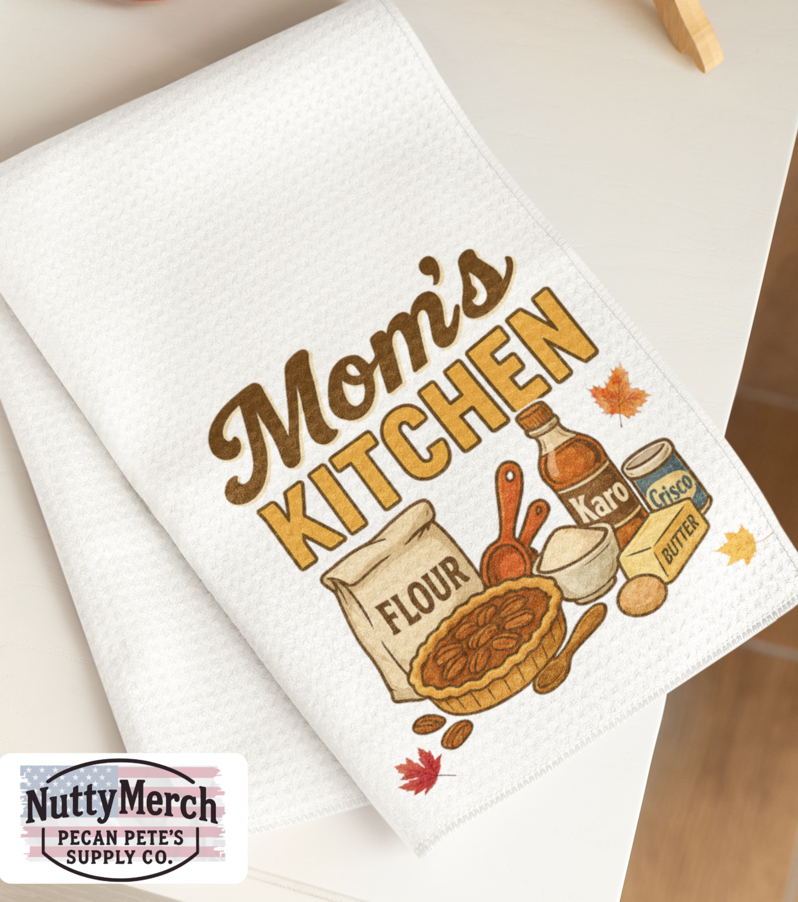 White towel with 'Mom's Kitchen' design featuring baking items on a kitchen counter.