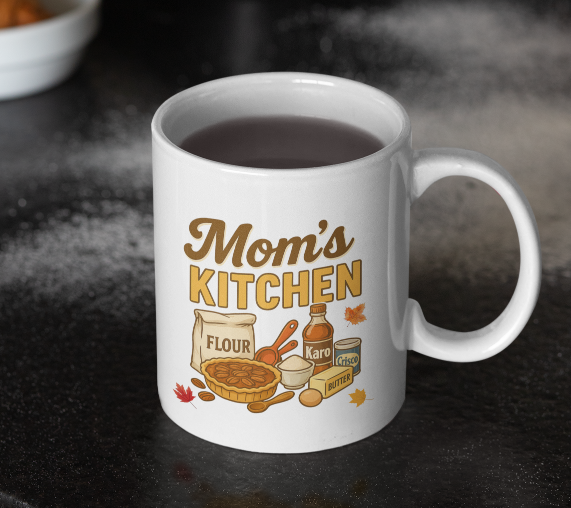 White mug with 'Mom's Kitchen' design featuring cooking items on a dark surface.