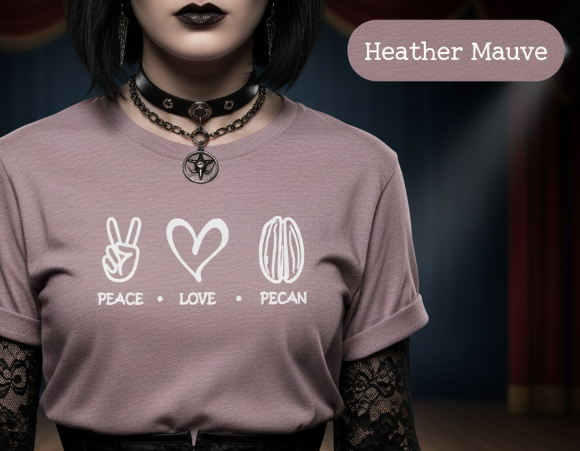 A person wearing a Heather Mauve graphic t-shirt with white printed icons and text ('PEACE • LOVE • PECAN'), styled with black lace sleeves and a black corset in a dark, moody stage setting.