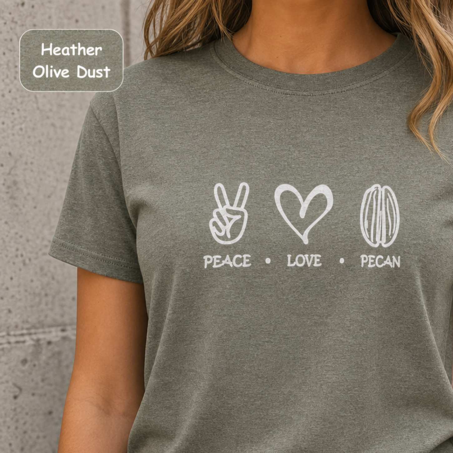 A woman wearing a heather olive dust t-shirt with a white graphic print of peace, love, and pecan symbols with the text 'PEACE • LOVE • PECAN'.