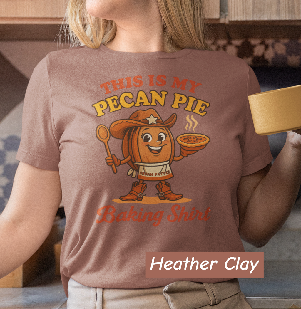 Ladies tee featuring cartoon Pecan Pattie wearing apron and hat, holding a pie and spoon, with the phrase ‘This Is My Pecan Pie Baking Shirt’ above and below her.”