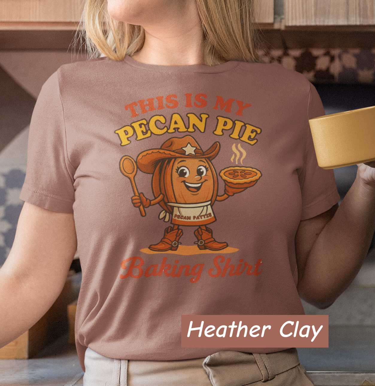 Ladies tee featuring cartoon Pecan Pattie wearing apron and hat, holding a pie and spoon, with the phrase ‘This Is My Pecan Pie Baking Shirt’ above and below her.”