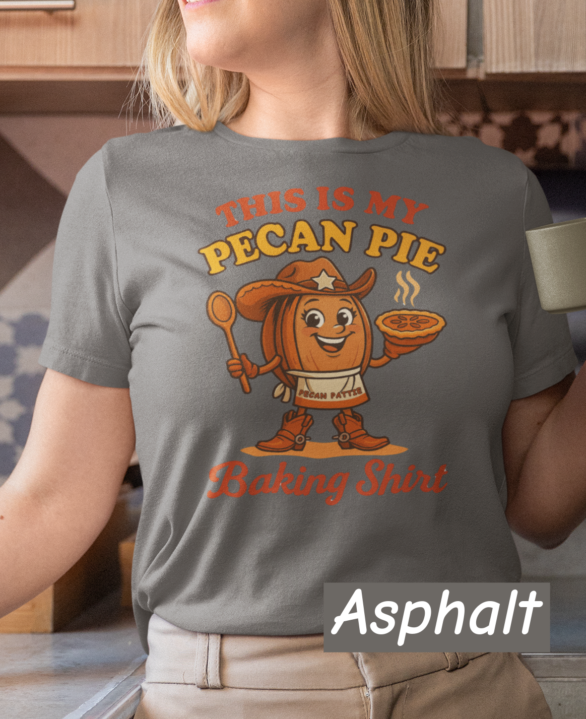 Ladies tee featuring cartoon Pecan Pattie wearing apron and hat, holding a pie and spoon, with the phrase ‘This Is My Pecan Pie Baking Shirt’ above and below her.”