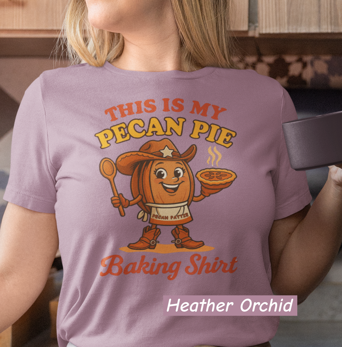 Ladies tee featuring cartoon Pecan Pattie wearing apron and hat, holding a pie and spoon, with the phrase ‘This Is My Pecan Pie Baking Shirt’ above and below her.”