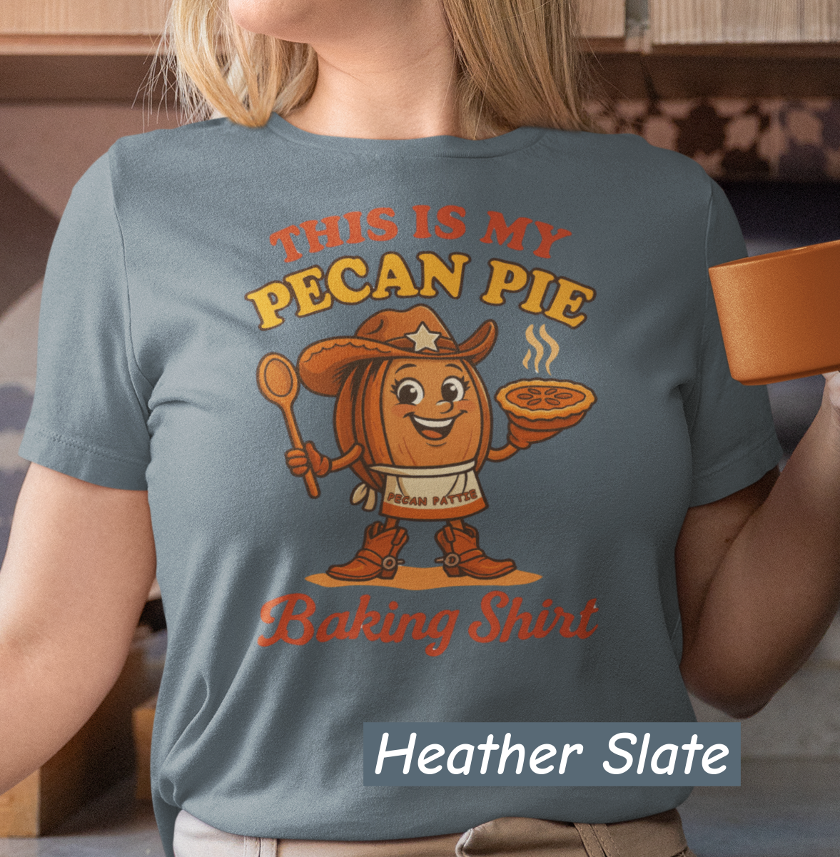 Ladies tee featuring cartoon Pecan Pattie wearing apron and hat, holding a pie and spoon, with the phrase ‘This Is My Pecan Pie Baking Shirt’ above and below her.”