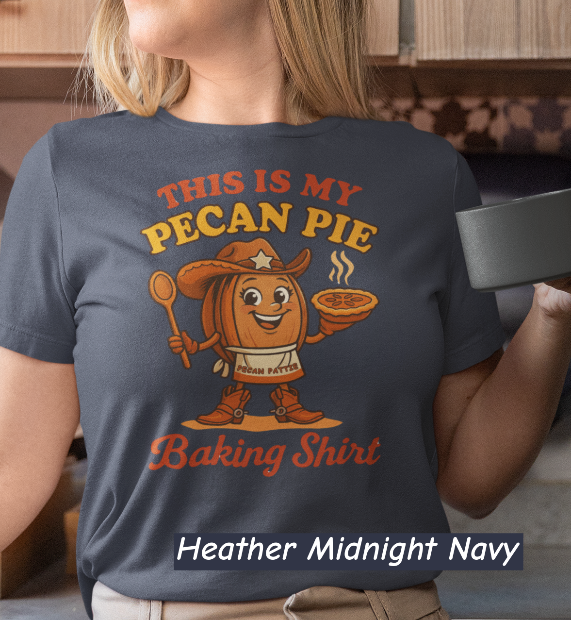 Ladies tee featuring cartoon Pecan Pattie wearing apron and hat, holding a pie and spoon, with the phrase ‘This Is My Pecan Pie Baking Shirt’ above and below her.”