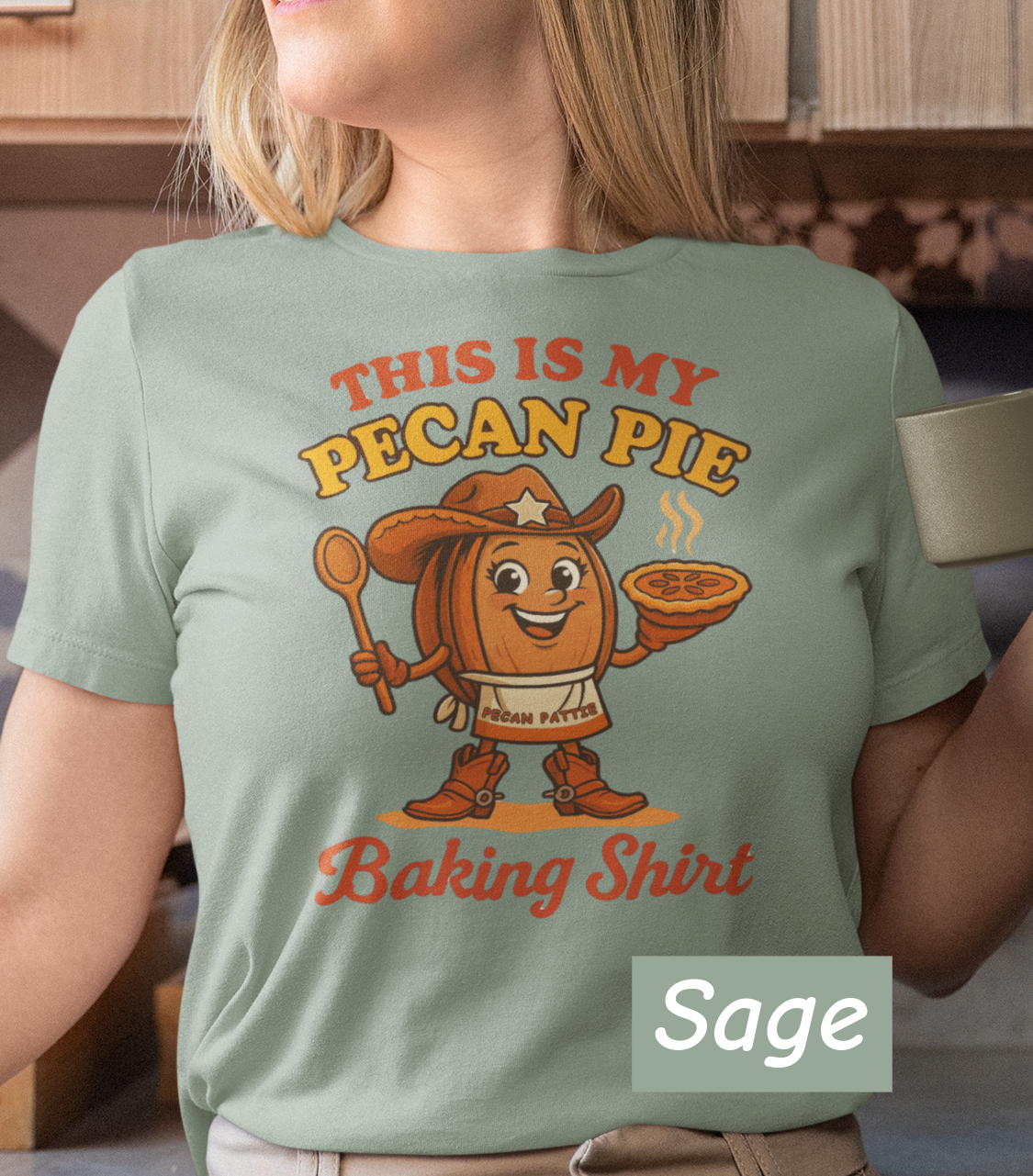 Ladies tee featuring cartoon Pecan Pattie wearing apron and hat, holding a pie and spoon, with the phrase ‘This Is My Pecan Pie Baking Shirt’ above and below her.”