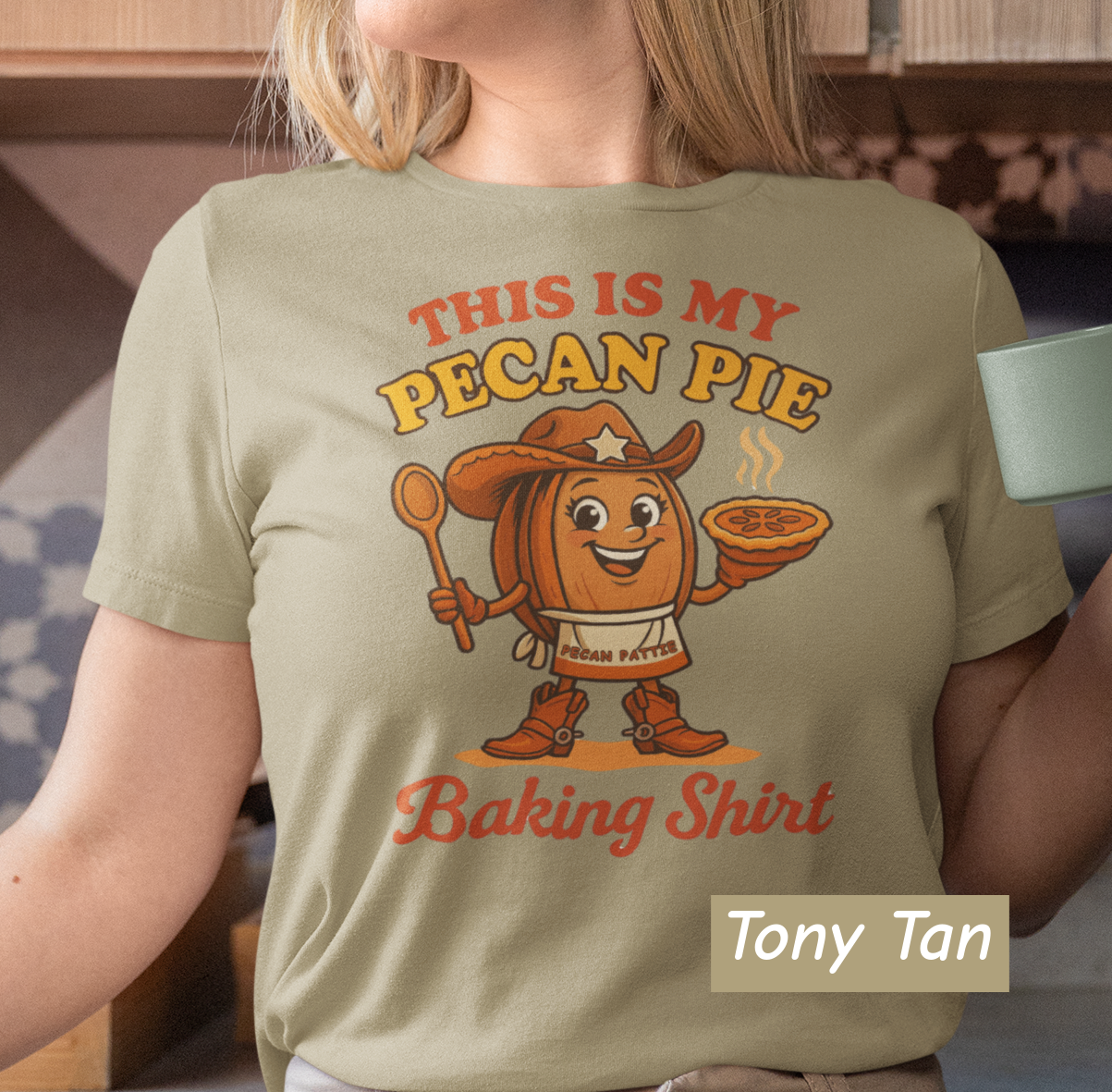 Ladies tee featuring cartoon Pecan Pattie wearing apron and hat, holding a pie and spoon, with the phrase ‘This Is My Pecan Pie Baking Shirt’ above and below her.”