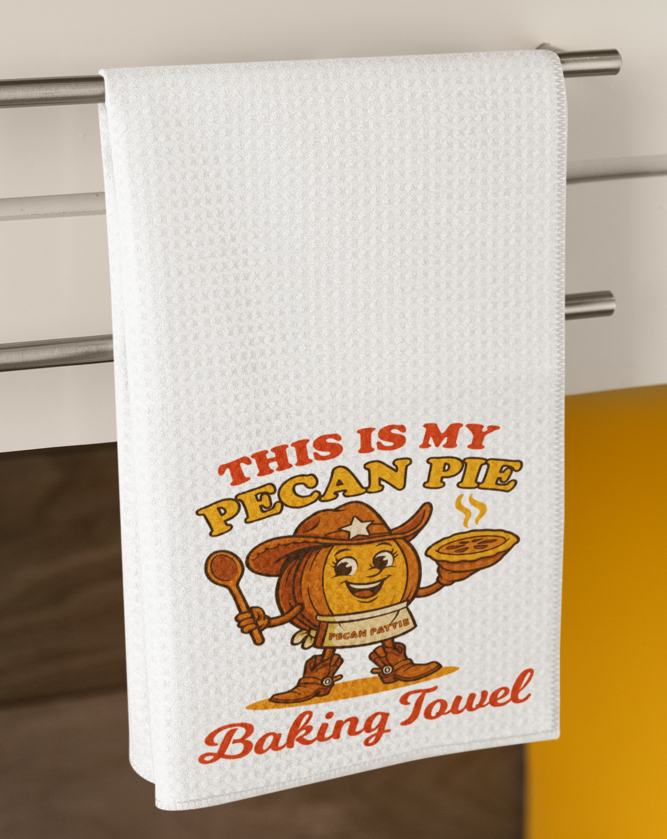 Illustration of Pecan Pattie, a smiling cowgirl pecan character in boots and hat, holding a steaming pie with the phrase “This Is My Pecan Pie Baking Towel” in bold retro lettering.