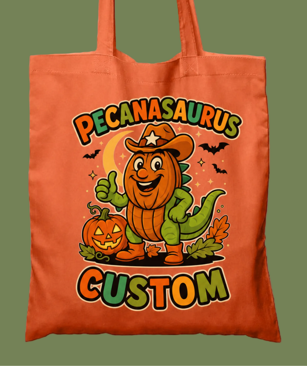 An orange canvas tote bag featuring a custom graphic of a smiling Pecanasaurus character in a cowboy hat next to a jack-o'-lantern, with the text 'PECANASaurus CUSTOM' printed on the front.