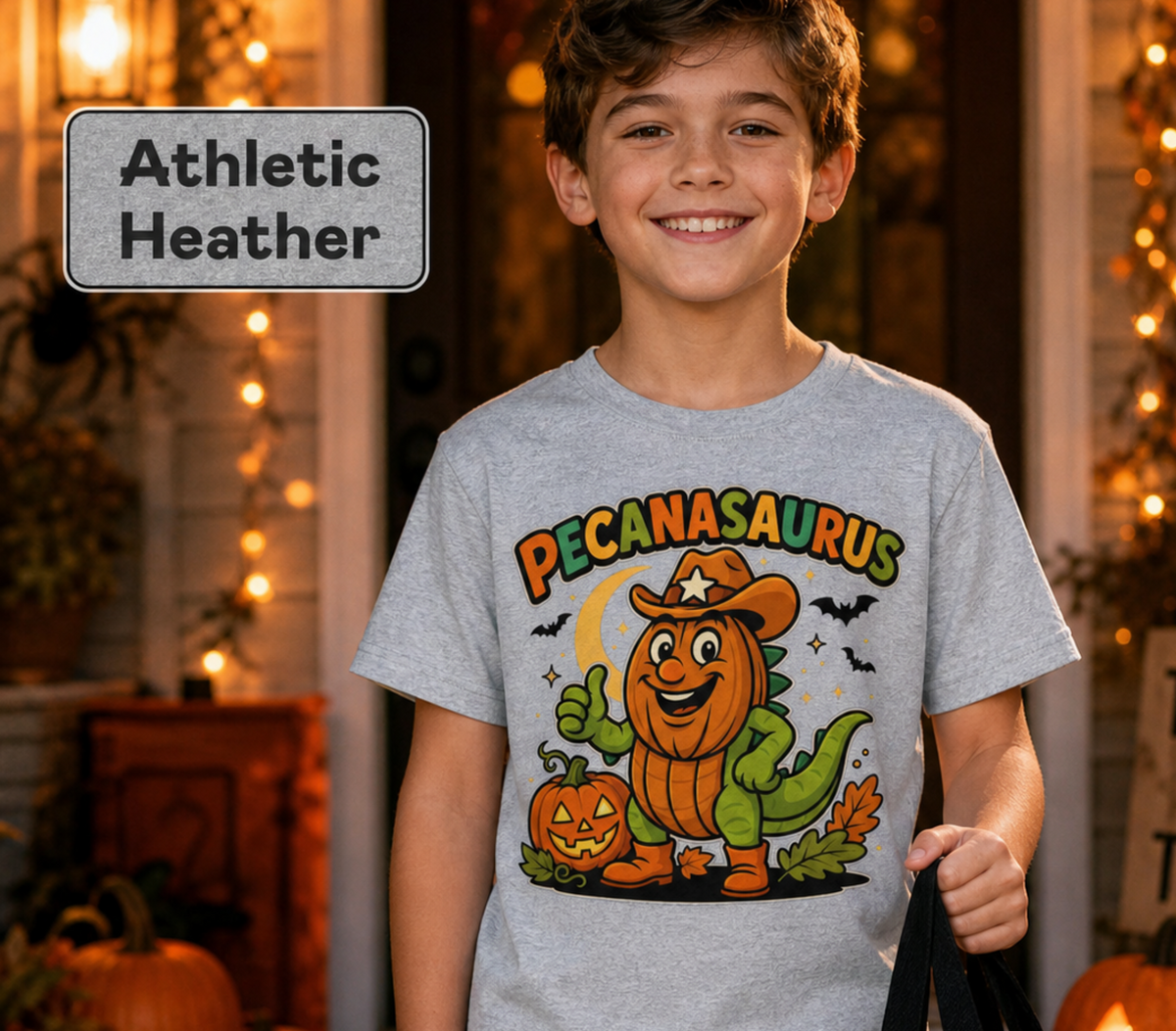 Athletic Heather t-shirt with a Halloween graphic featuring the word "PECANASAURUS" above a green dinosaur wearing a pumpkin head, cowboy hat, and boots, set against a dark night background with a crescent moon, bats, and jack-o'-lanterns.
