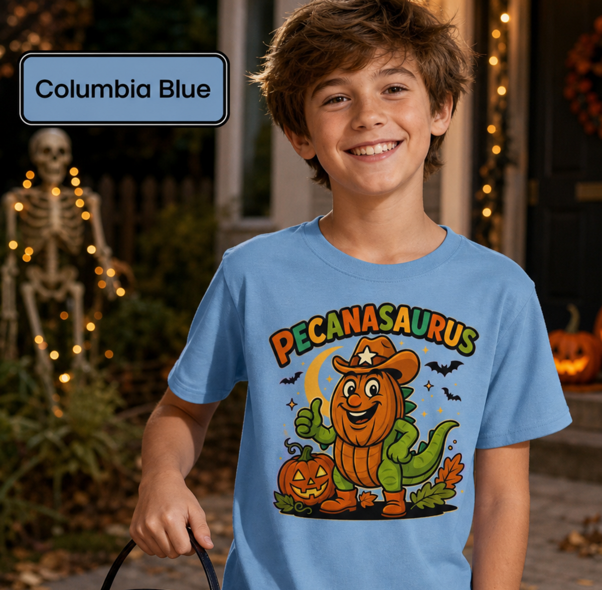 Blue t-shirt with a Halloween graphic featuring the word "PECANASAURUS" above a green dinosaur wearing a pumpkin head, cowboy hat, and boots, set against a dark night background with a crescent moon, bats, and jack-o'-lanterns.