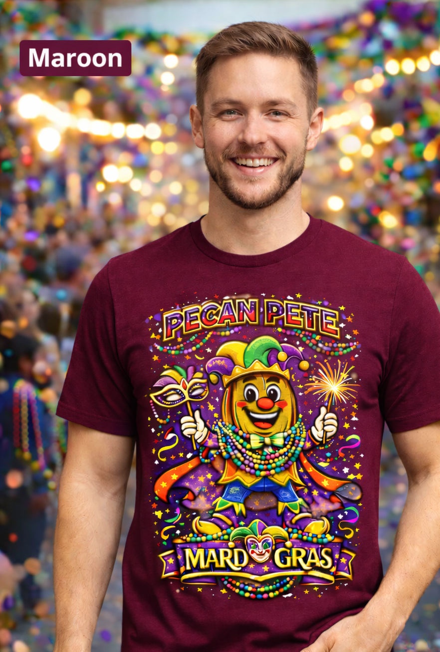 Smiling model wearing a colorful Mardi Gras Pecan Pete graphic T-shirt, featuring a festive jester pecan character with beads, mask, sparkler, and parade confetti, photographed against a lively Mardi Gras celebration background.