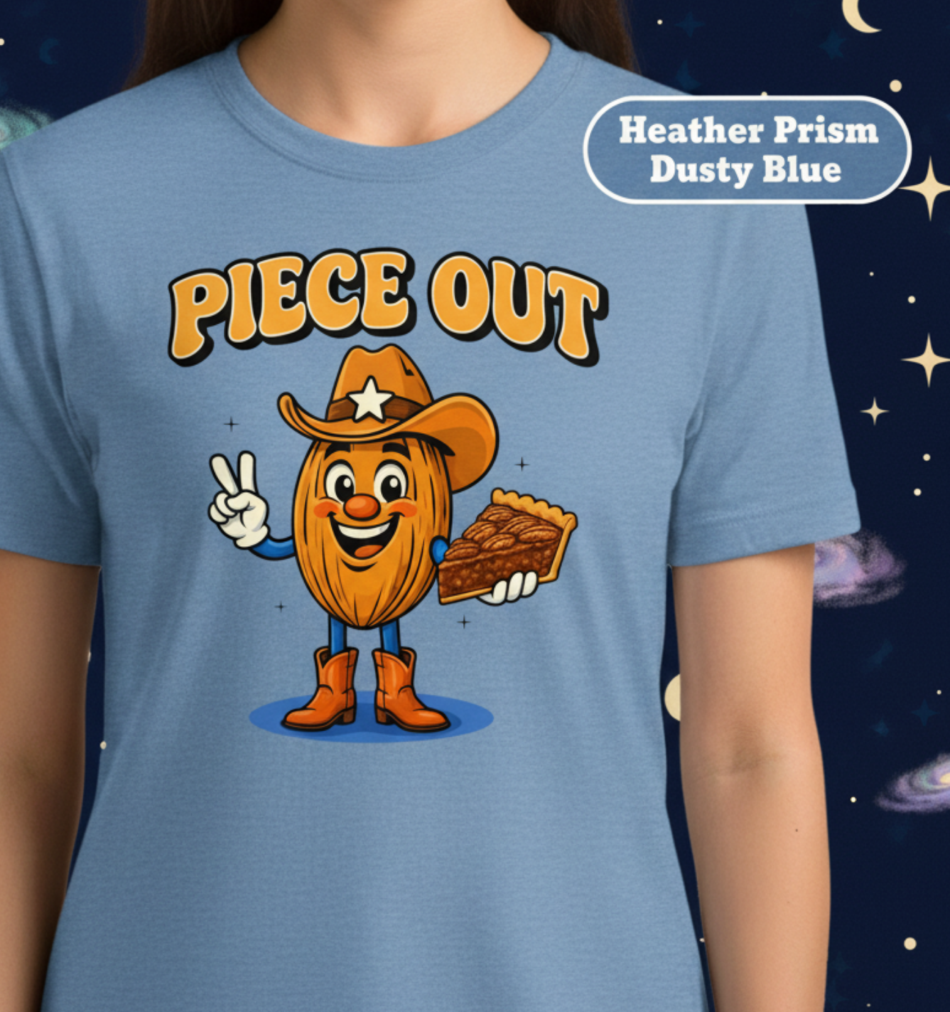 A person wearing a dusty blue graphic T-shirt against a dark starry space background. The shirt has a cartoon nut character wearing a cowboy hat and boots with the text 'PIECE OUT' above it.