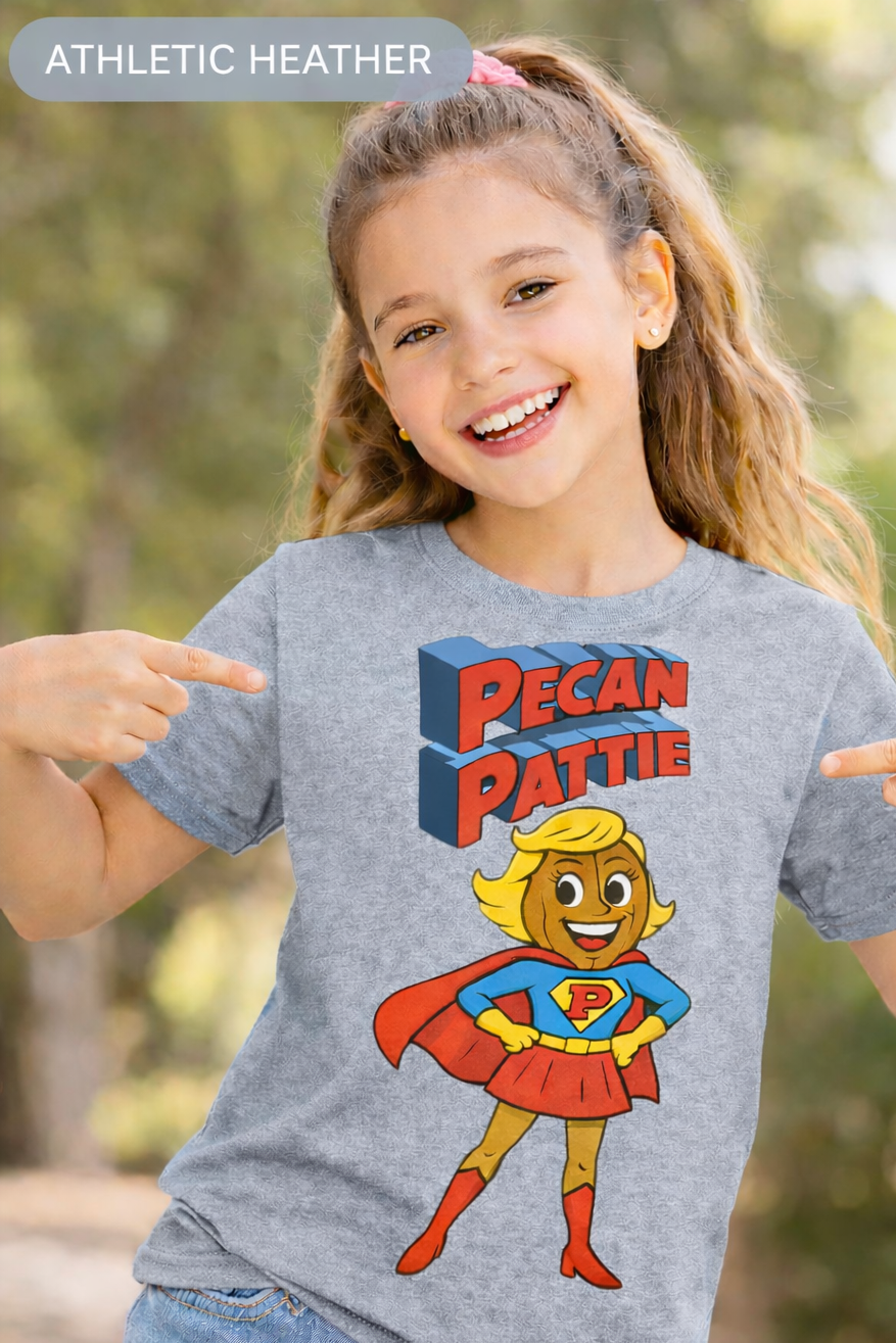Happy girl modeling a Bella+Canva youth T-shirt featuring the Super Pecan Pattie cartoon superhero design, pointing at the graphic with an outdoor background.