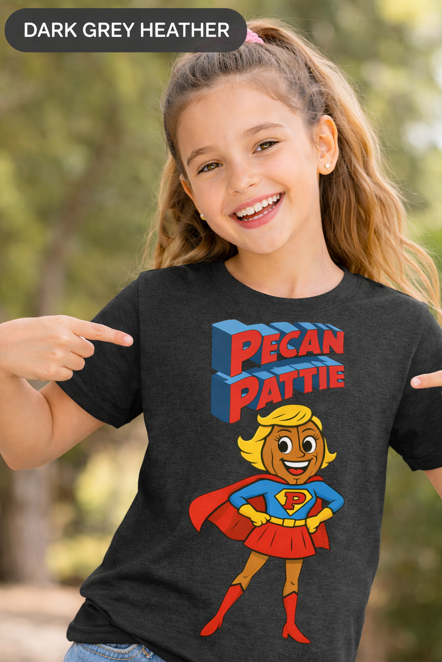 Happy girl modeling a Bella+Canva youth T-shirt featuring the Super Pecan Pattie cartoon superhero design, pointing at the graphic with an outdoor background.