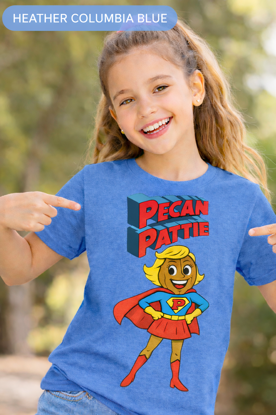 Happy girl modeling a Bella+Canva youth T-shirt featuring the Super Pecan Pattie cartoon superhero design, pointing at the graphic with an outdoor background.