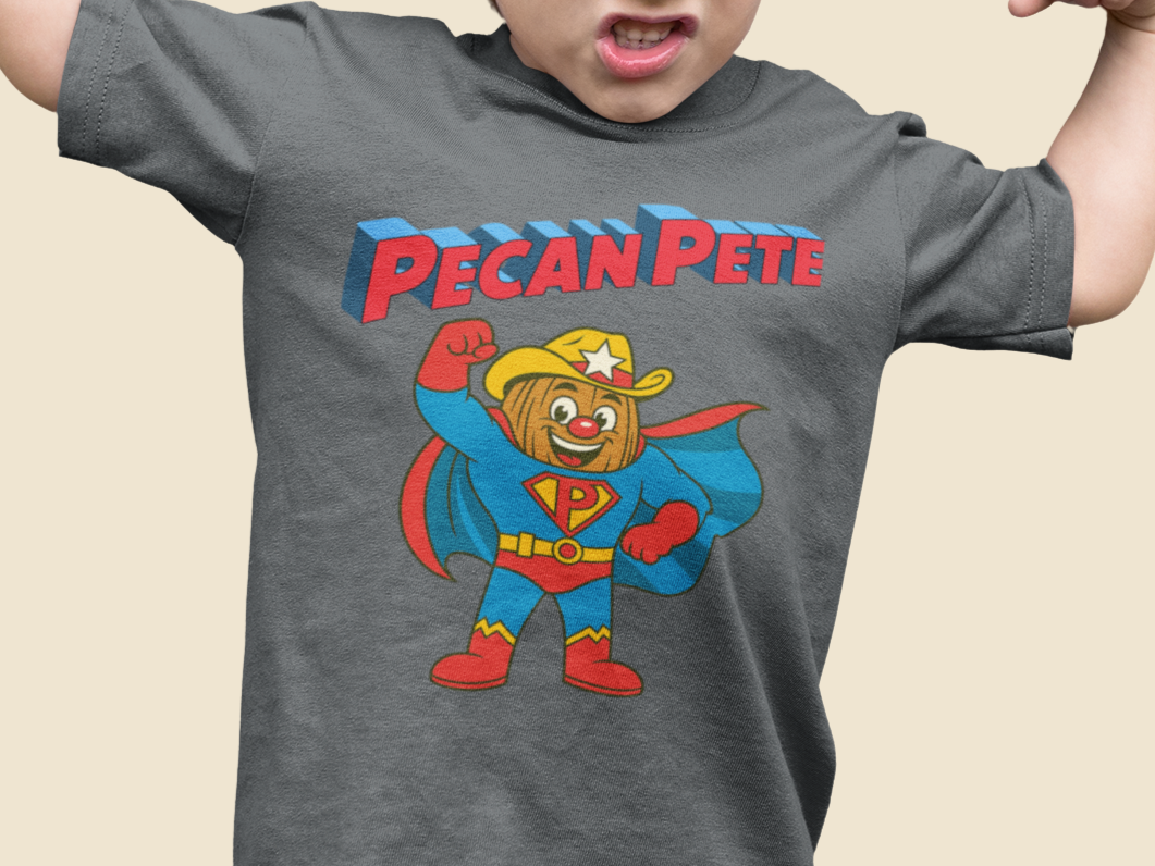 “Cartoon superhero Pecan Pete in blue and red costume with cape and cowboy hat on NuttyMerch youth tee – retro comic style superhero design.”