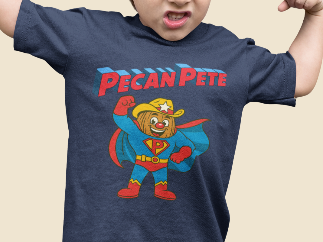 “Cartoon superhero Pecan Pete in blue and red costume with cape and cowboy hat on NuttyMerch youth tee – retro comic style superhero design.”
