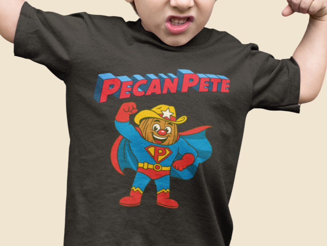 “Cartoon superhero Pecan Pete in blue and red costume with cape and cowboy hat on NuttyMerch youth tee – retro comic style superhero design.”