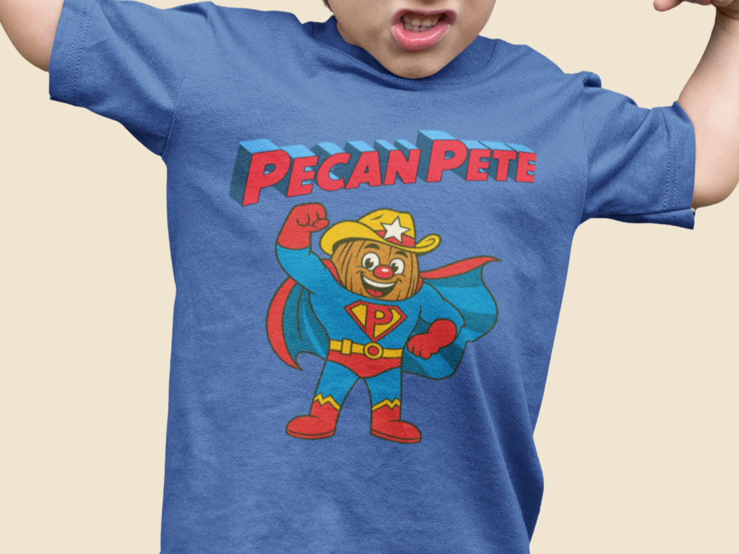 “Cartoon superhero Pecan Pete in blue and red costume with cape and cowboy hat on NuttyMerch youth tee – retro comic style superhero design.”