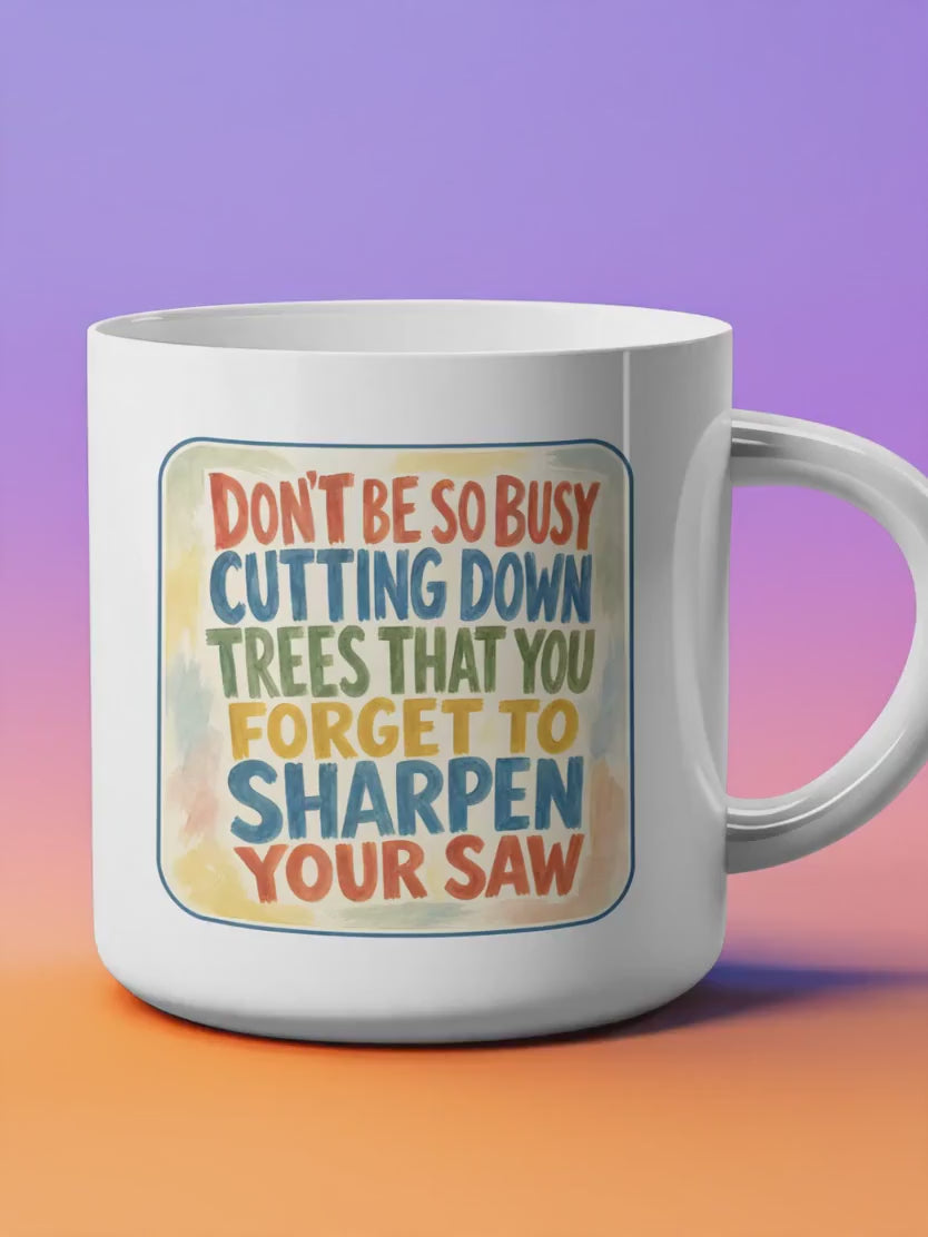 A white ceramic 11 oz coffee mug featuring a colorful, rustic graphic with the text "DON'T BE SO BUSY CUTTING DOWN TREES THAT YOU FORGET TO SHARPEN YOUR SAW." The typography is a mix of bold blue, green, and orange capital letters set against a soft, warm-toned watercolor background.