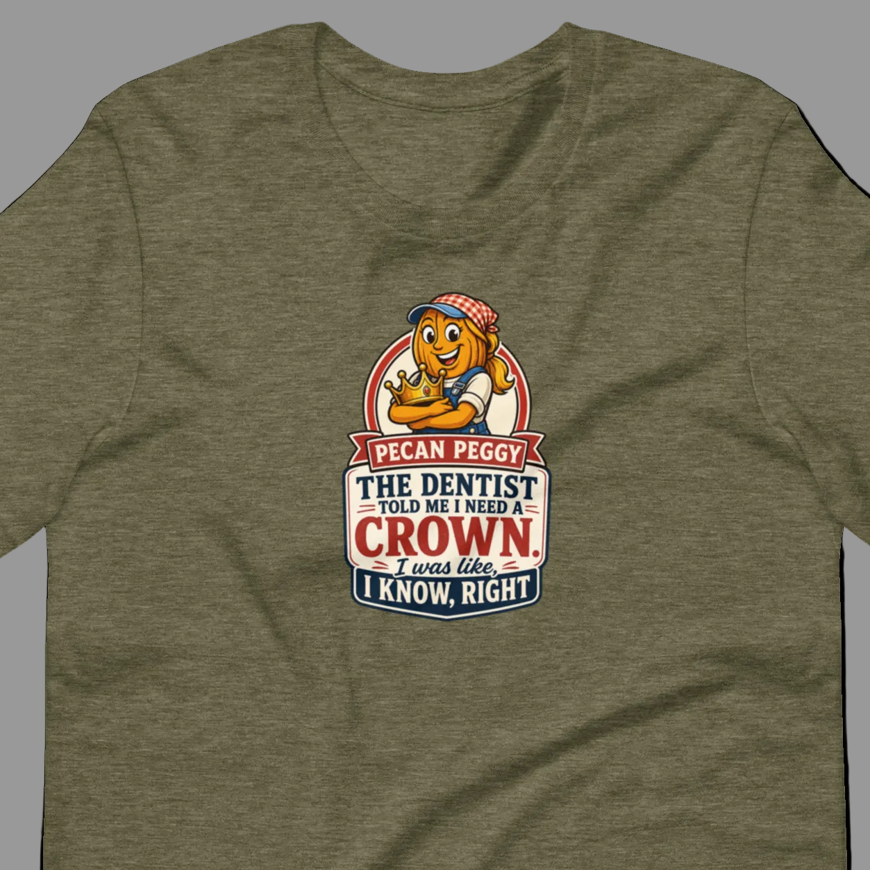 A heather olive green short-sleeve t-shirt with a vintage-style cartoon graphic on the chest. The graphic features a lion wearing a dentist hat and the text 'I CAN PEGGY THE DENTIST IS MY MIGHT CROWN.